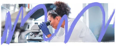 Researcher in lab wearing a white lab coat looking through microscope.